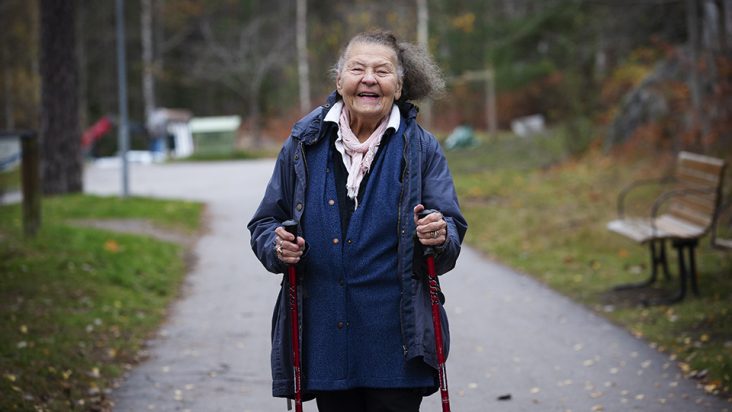 Bild på äldre kvinna som ler och går med gångstavar 
